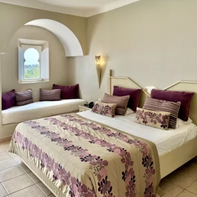 Chambre triple au Djerba Resort alliant confort moderne et architecture tunisienne avec banquette sous arche.