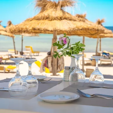 Table dressée face à la mer Méditerranée sous les parasols en paille de l'hôtel Djerba Golf.