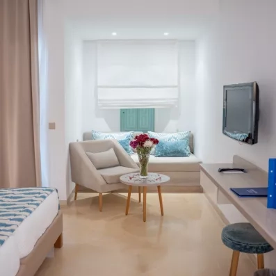 Coin salon lumineux d'une chambre à l'hôtel Ulysse Djerba avec fauteuil gris et bouquet de fleurs.