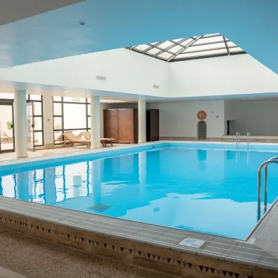 Piscine intérieure chauffée de l'hôtel Ulysse Djerba avec grandes baies vitrées et architecture élégante.