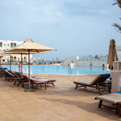 Large piscine extérieure de l'hôtel Ulysse Djerba avec pont décoratif et palmiers sous le soleil.