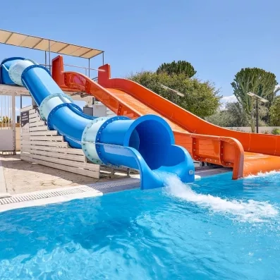 toboggans couvert bleu et blanc, découvert rouge en fonctionnement, arbres derrière, oliviers, cactus, ciel bleu 