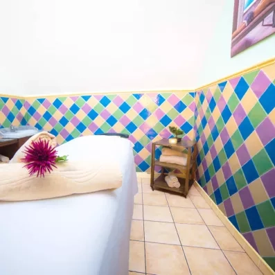 Une salle de soin avec une table de massage devant un mur de carreaux multicolores.