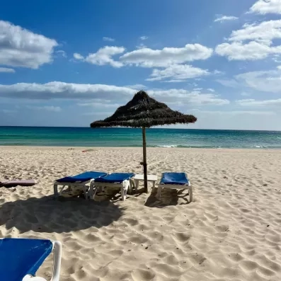Plage de sable fin avec transats bleus et parasol en chaume