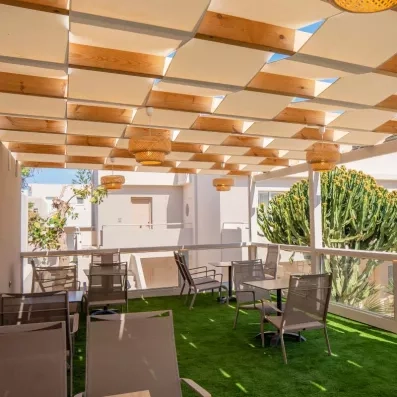 bar terrasse, luminaires tressés, grands cactus, plantes bâtiments blancs typiques, tables et chaises, sol en gazon