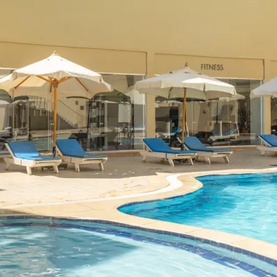 Piscine extérieure relaxante avec transats bleus et parasols blancs près de la salle de fitness.