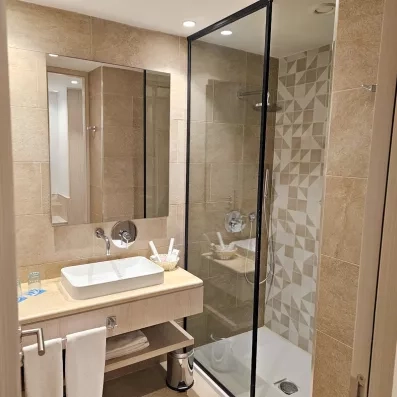 Salle de bain moderne de l'hôtel Mondi Club One Resort Jockey à Monastir, Tunisie, avec douche à l'italienne et vasque design.