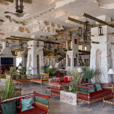 Salon traditionnel avec bancs en bois sculpté, lanternes suspendues et murs en pierre texturée.