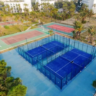Vue aérienne des terrains de tennis et de padel bleus entourés de palmiers au Mondi Club One Resort Jockey Monastir.