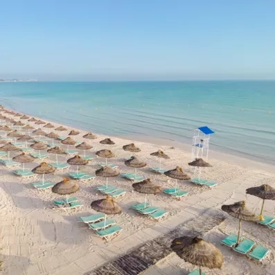 Plage privée de sable fin avec parasols en paille et chaises longues au Mondi Club One Resort Jockey, vue sur la mer Méditerranée.