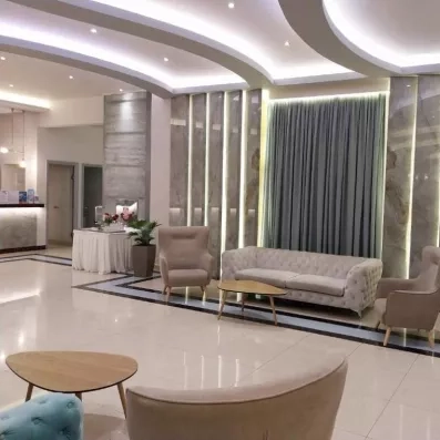 hall entrée avec canapées fauteuils et tables basses en bois, déco marbre grise et blanche, lumière au plafond, verres posés sur une table avec une nappe