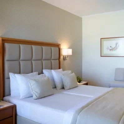 La chambre avec grand lit double, une tête de lit en tissu beige et en bois