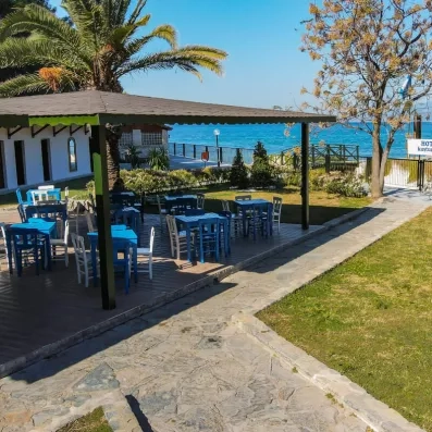 Un petit coin repas avec des tables bleues, situé dans un jardin face à une crique.