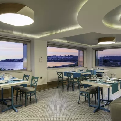 Le restaurant intérieur mettant en avant le panorama sur la côte illuminée par le coucher du soleil.