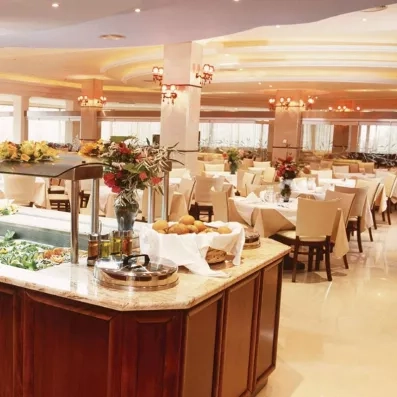 buffet riche et varié, pains dans un grande corbeille posée sur le plan de travail, crudités, condiments, plante, tables et chaises beiges, nappes