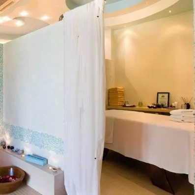 Spa, table de massage cachée par un grand rideau blanc, serviettes, bâtons d'encens, diplôme encadré posé sur une petite table