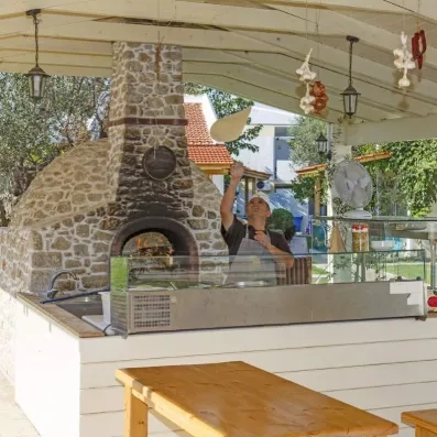 pizzaiolo devant le four à pizza qui prépare une pizza et la lance dans les airs, gousses dail accrochées au plafond