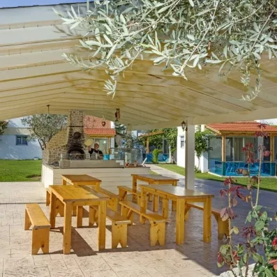 restaurant de pizza, pizzaiolo qui prépare une pizza, terrasse couverte, table et bancs en bois, oliviers