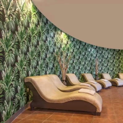 Un espace de relaxation zen avec des chaises longues devant un mur au motif de feuillage tropical.