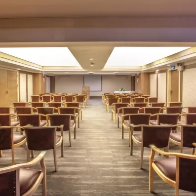 Une salle de réunion spacieuse, organisée avec des rangées de fauteuils et un écran de projection.