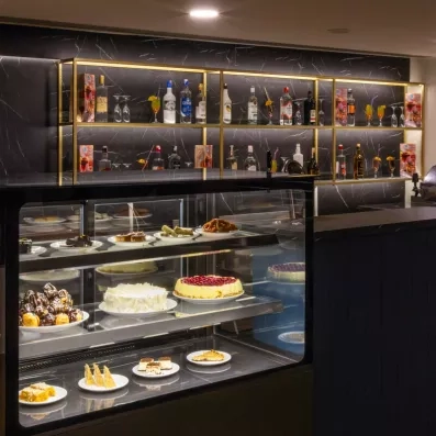 Un bar à desserts et digestifs chic avec une vitrine de gâteaux et une étagère de bouteilles.