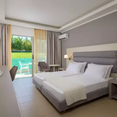 lit double et tables de nuit, grande tête de lit grise, baie vitrée qui donne sur un balcon, avec deux gros rideaux