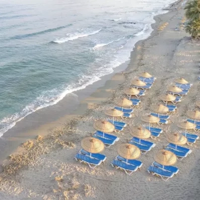 Des rangées de parasols en paille et de transats sur une plage de sable.