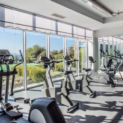 Une salle de fitness lumineuse avec des vélos faisant face à une baie vitrée vue sur mer.