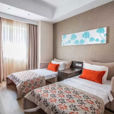 Une chambre avec des lits jumeaux, décorés de coussins sous un tableau d'art moderne.