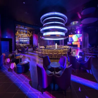 Discothèque, lumière violette, tables et fauteuils, bar circulaire au centre et emplacement pour un dj