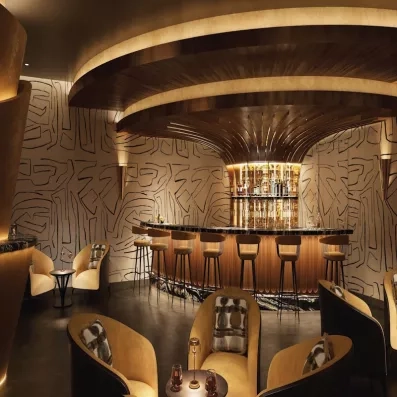 Bar doré, lumière tamisée, tabourets de bar, fauteuils confortables, bouteilles