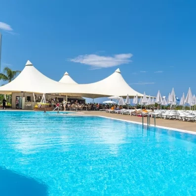 Une grande piscine bordée de nombreux transats, située juste à côté d'un bar extérieur.