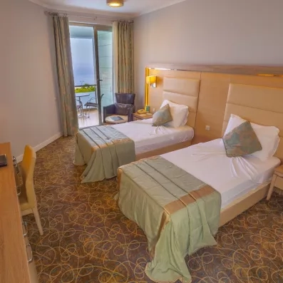 Une chambre avec deux lits jumeaux et un balcon offrant une vue sur la mer.