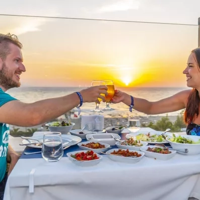 Un couple trinquant face à un magnifique coucher de soleil sur la mer.