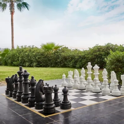 Un jeu d'échecs géant installé à l'extérieur sur une terrasse entourée de verdure.