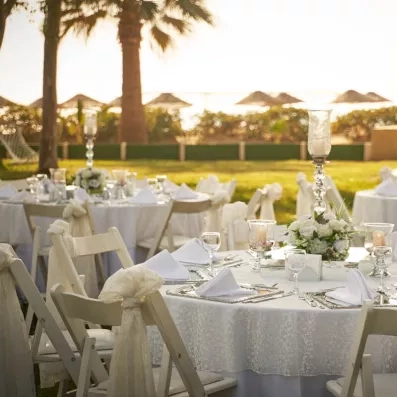 Un banquet élégante en plein air, avec des tables rondes dressées sous les palmiers.
