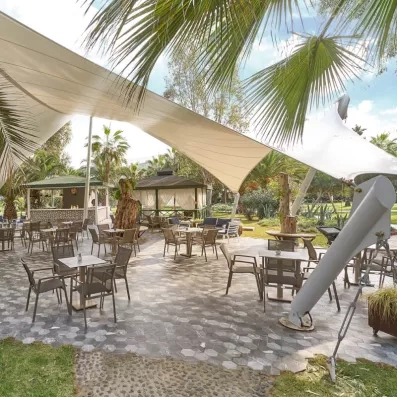 Une terrasse ensoleillée avec des tables et chaises sous une grande voile d'ombrage.