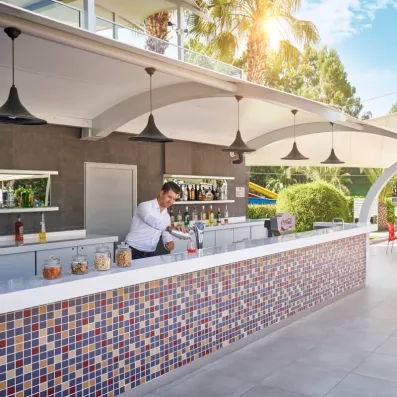 Un bar extérieur au design moderne et carrelé où un serveur prépare des boissons.