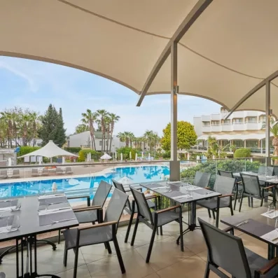 Une terrasse de restaurant surplombant une piscine, sous une tente tendue.
