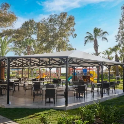 Un espace de restauration extérieur abrité, entouré de palmiers et de jardins.