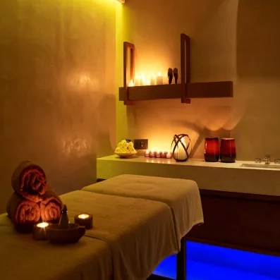 table de massage, serviettes enroulées et posées dessus, bougies, petites sculptures lumière tamisée, point d'eau