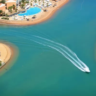 Vue aérienne d'un bateau rapide naviguant dans les lagunes turquoise du Mövenpick Resort à El Gouna.