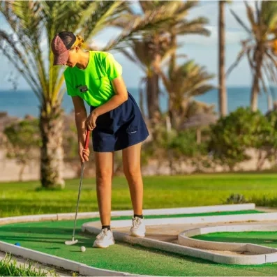 Jeune femme pratiquant le mini-golf sous les palmiers lors d'un séjour de vacances au Palm Azur.