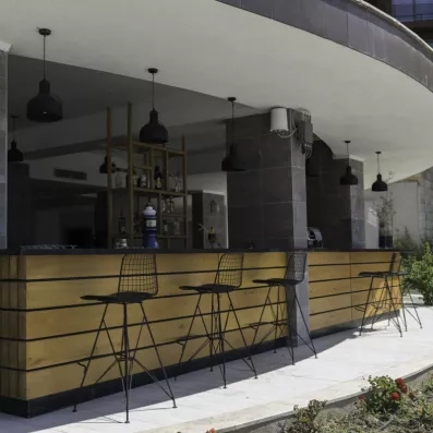 Un bar extérieur avec un comptoir en bois strié et de hautes chaises métalliques noires.