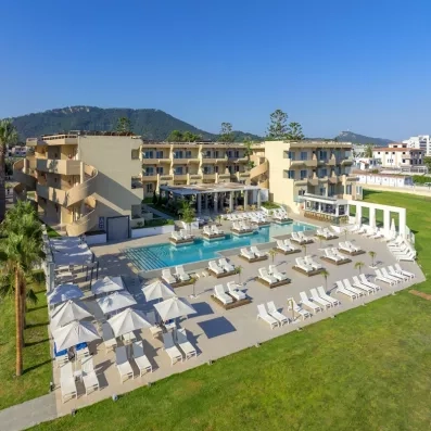 Vue d'ensemble beau temps, transats au bord de la piscine, parasols, palmiers, bâtiment de l'hôtel
