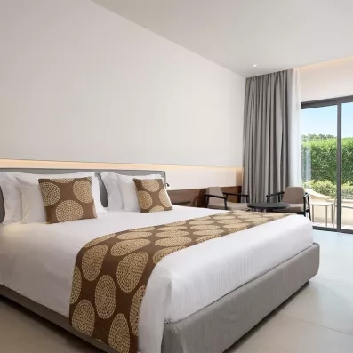 Chambre avec lit double et canapé, baie vitrée qui donne sur le balcon, petite télé posée sur une commode, grand miroir