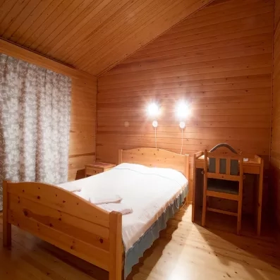 chambre cosy entièrement en bois, avec un lit double, deux lampes murales, un petit meuble pour enfant et une ambiance chaleureuse de chalet