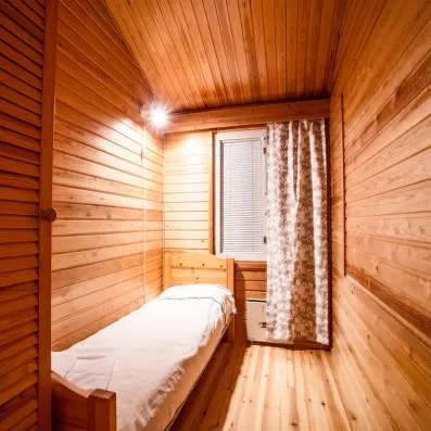  petite chambre individuelle entièrement en bois, avec un lit simple près d’une fenêtre voilée et une atmosphère chaleureuse et intimiste de chalet.