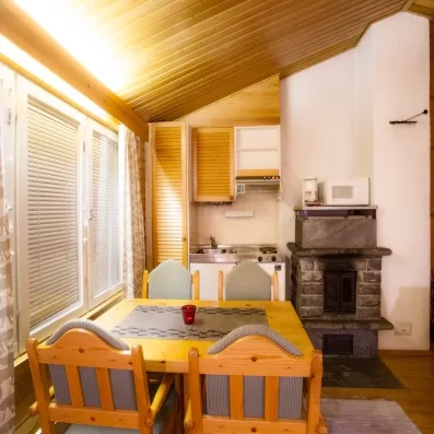 Il s’agit d’un espace salon‑salle à manger de style chalet, avec une table en bois, un coin kitchenette équipé, un poêle à bois et une ambiance chaleureuse et lumineuse.