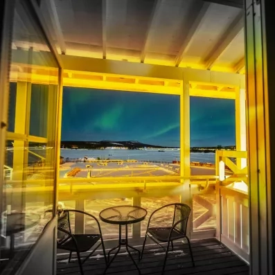 Aurores boréales visibles depuis un balcon enneigé au Grand Arctic Resort, spectacle naturel en Laponie suédoise.